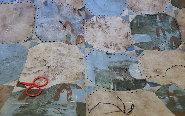 Closeup of a blue and gray quilt, with quilting in progress and a pair of red embroidery scissors.