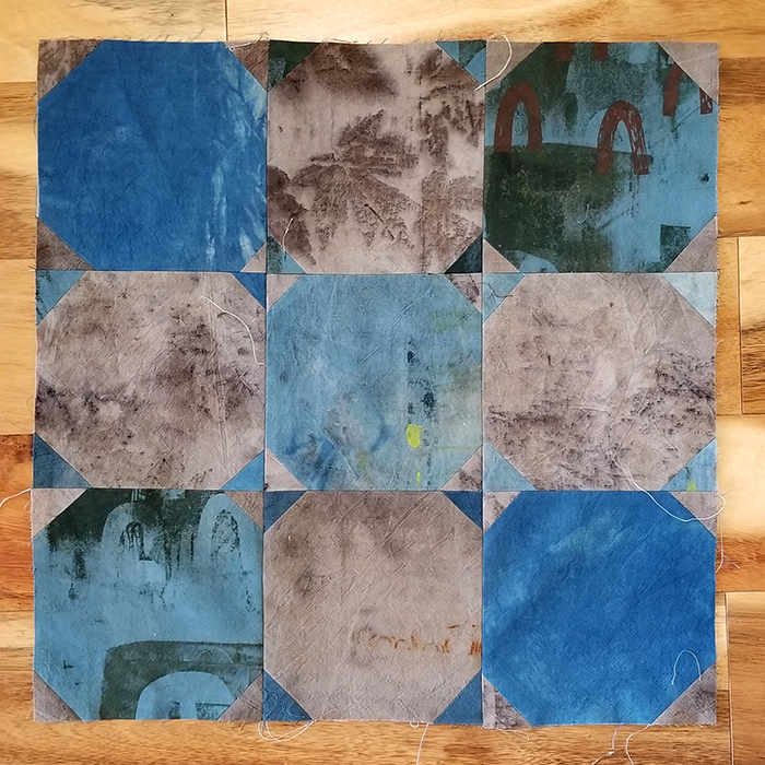 A nine-patch quilt square of blue and gray hand printed fabrics.