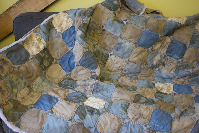 A blue and gray quilt jumbled on a couch.