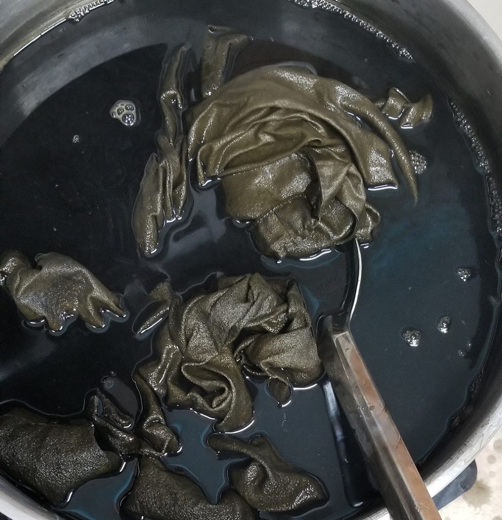 fabric floating in olive green dye in a steel pot