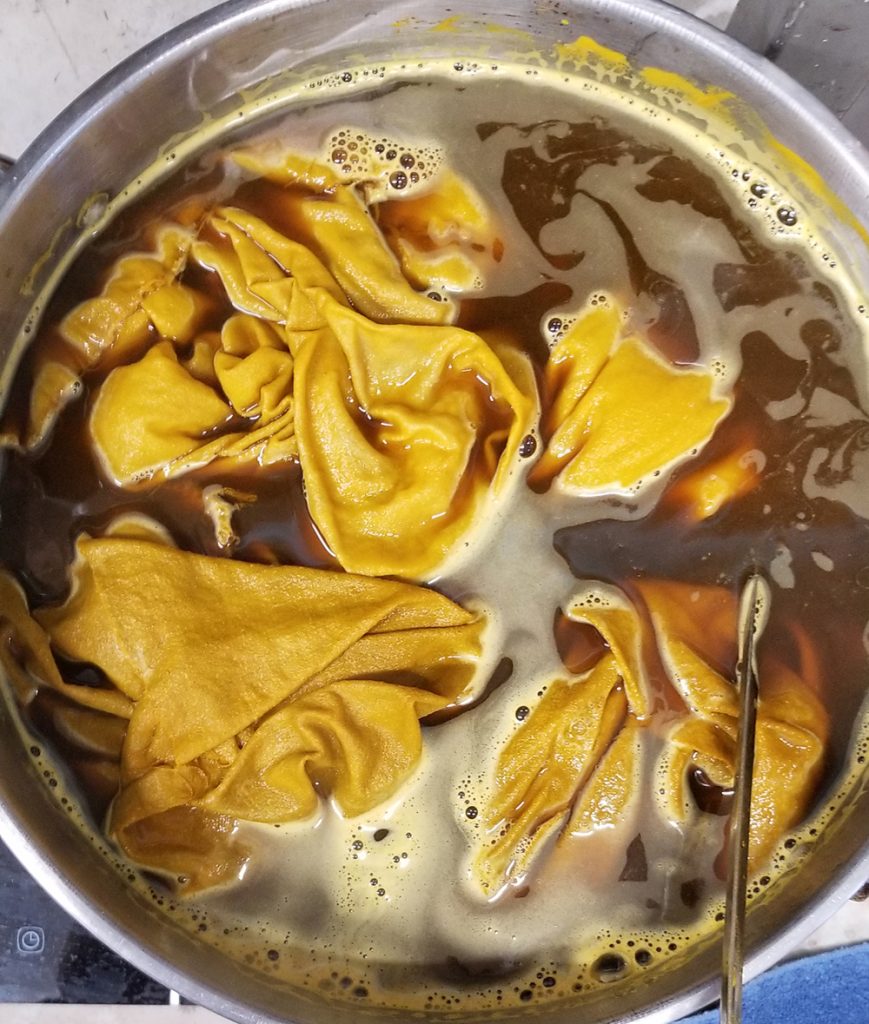 fabric floating in deep yellow dye in a steel pot