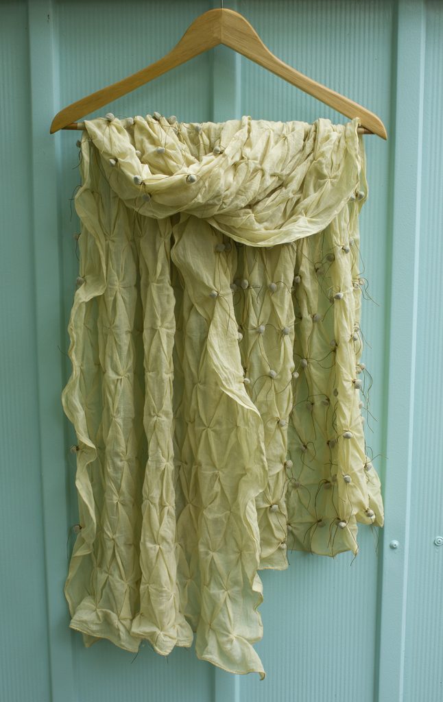 a pale yellow shawl hanging against a seafoam green steel garden shed
