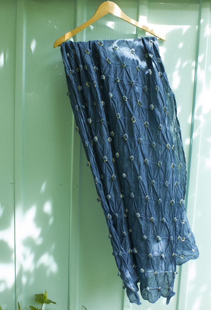 indigo dyed fabric covered in tiny yellow puckers, hanging against a seafoam green garden shed