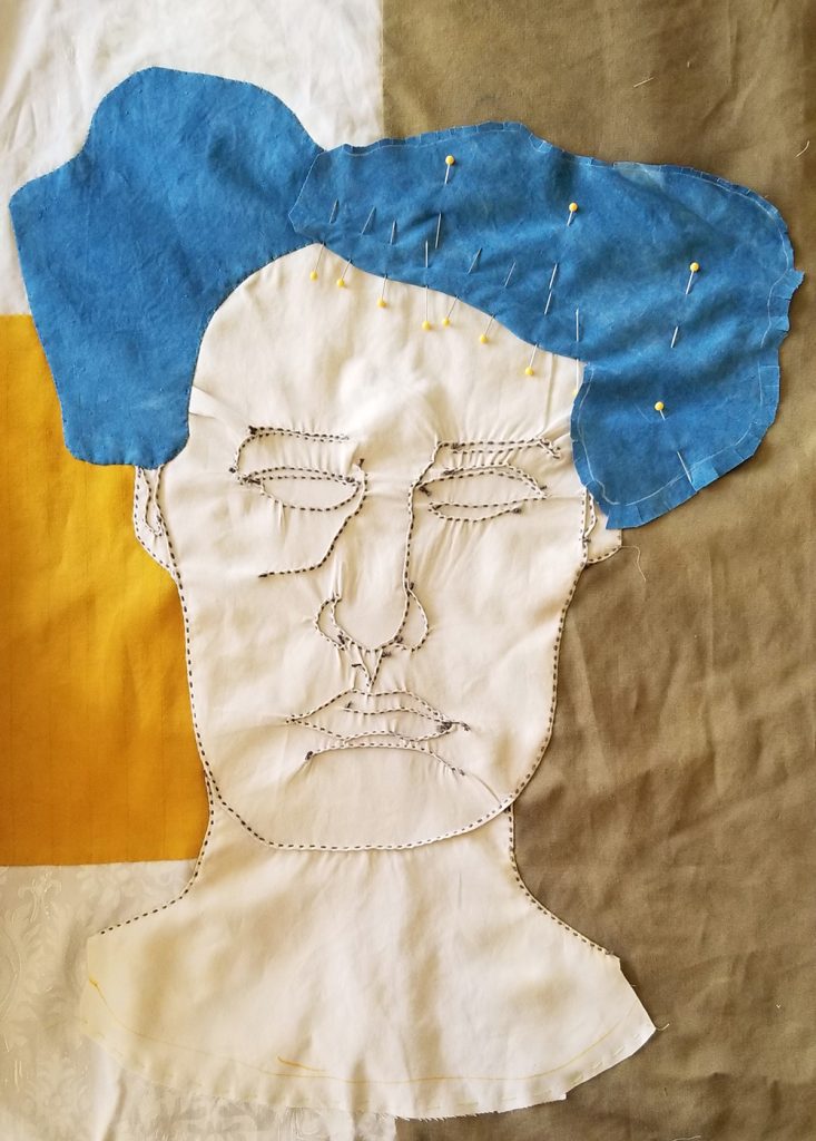 a hand stitched portrait in progress, white face with blue hair on a yellow and olive background