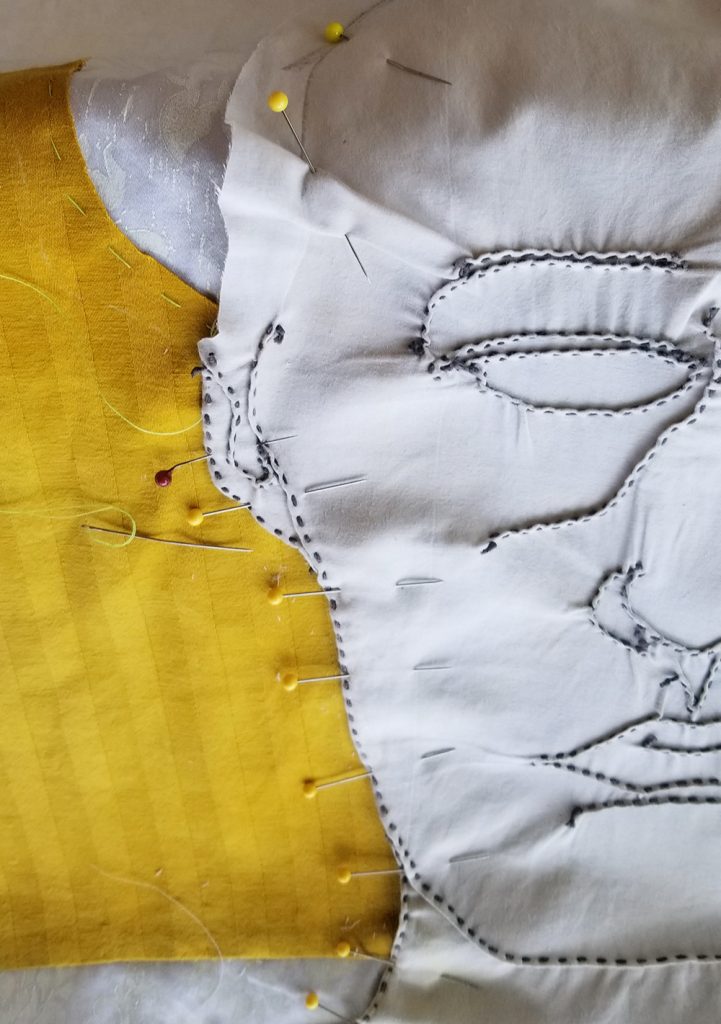 yellow and white fabric pinned together with a stitched drawing of half a face showing